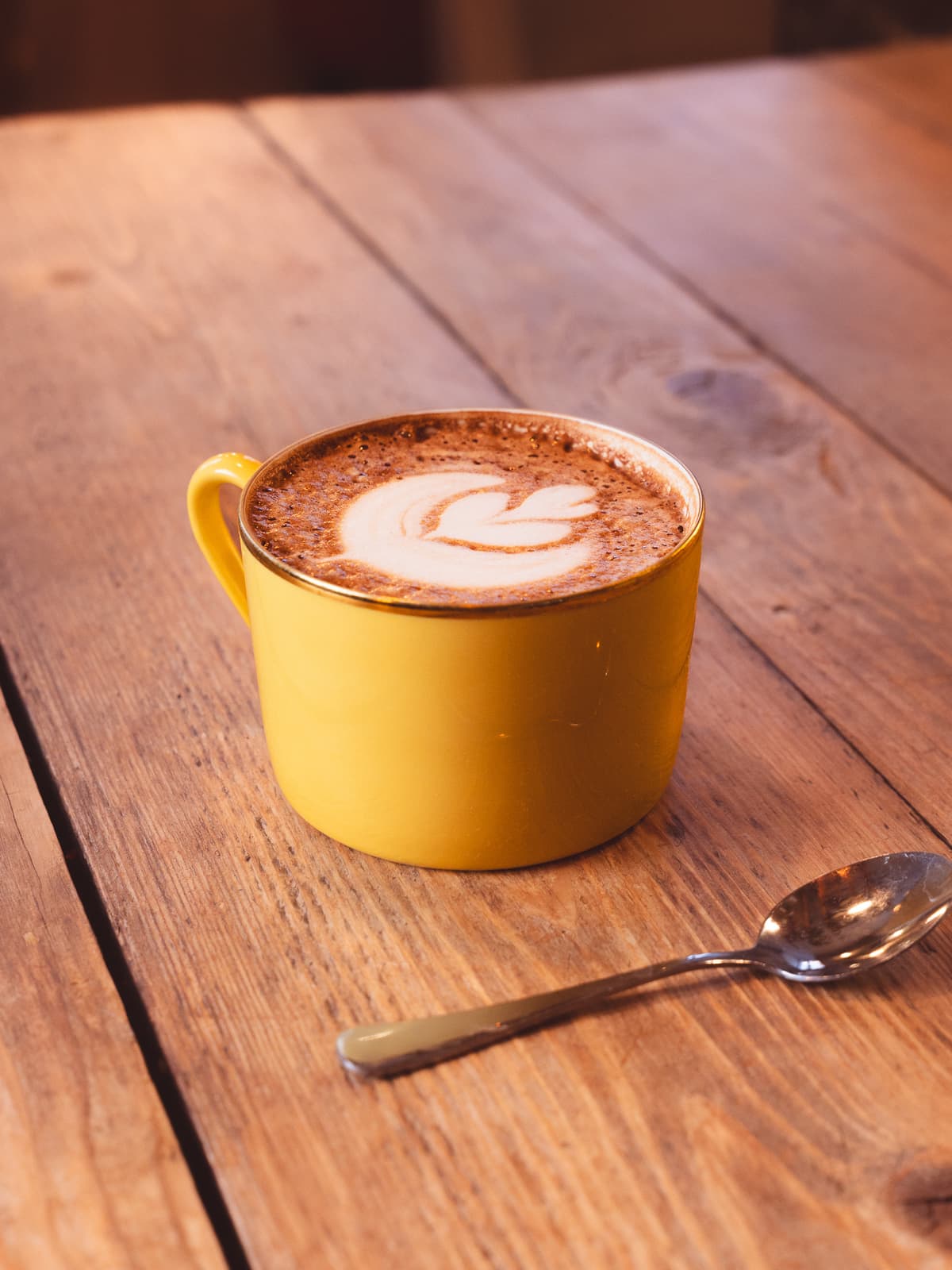 Hot chocolate with latte art in a yellow cup on a wooden table