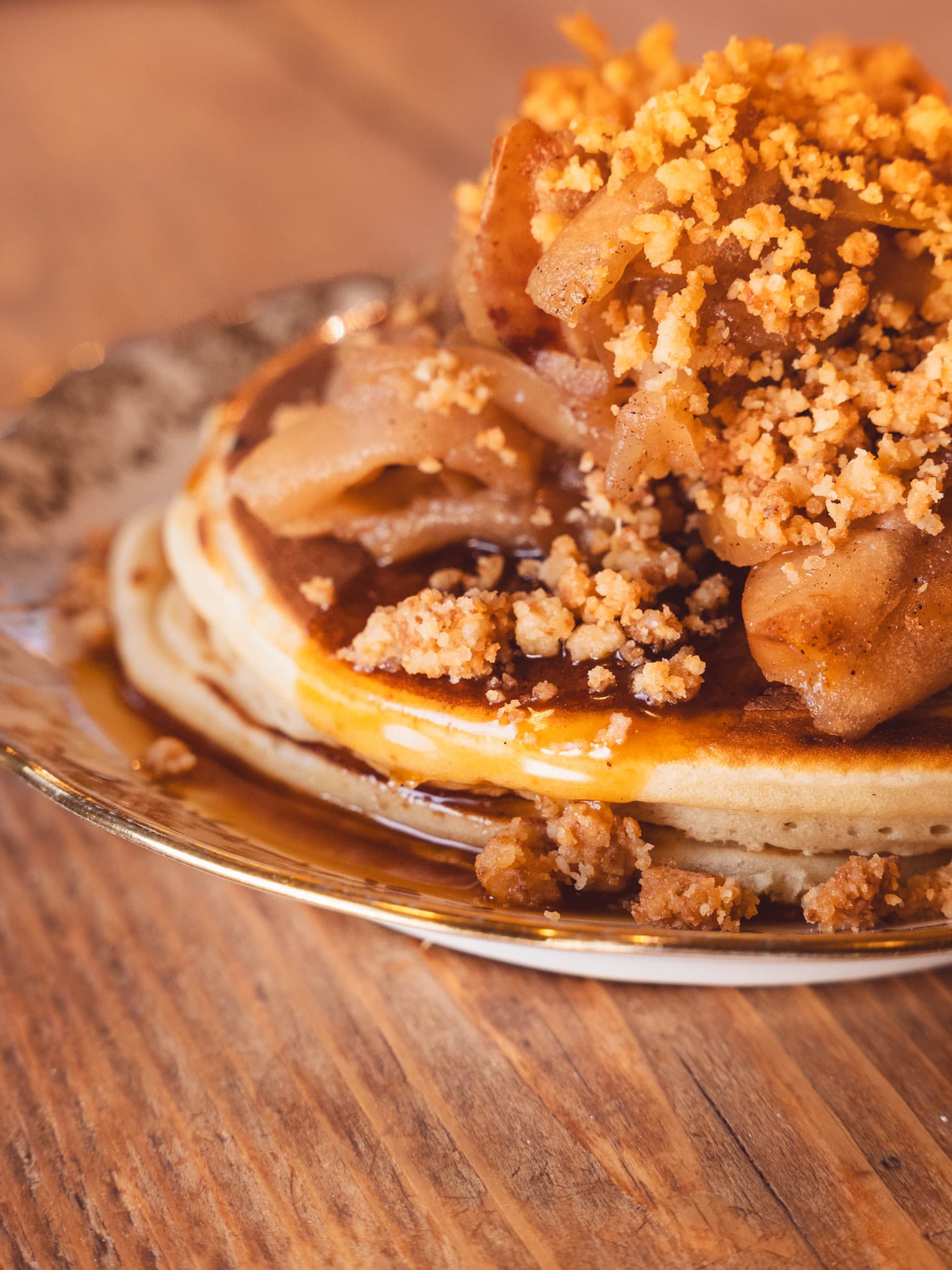 Stack of pancakes topped with baked apples, coconut crumble and salted caramel