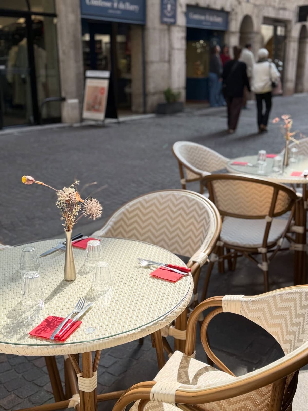 Café terrace with rattan chairs and set tables on a cobbled street in Annecy's old town